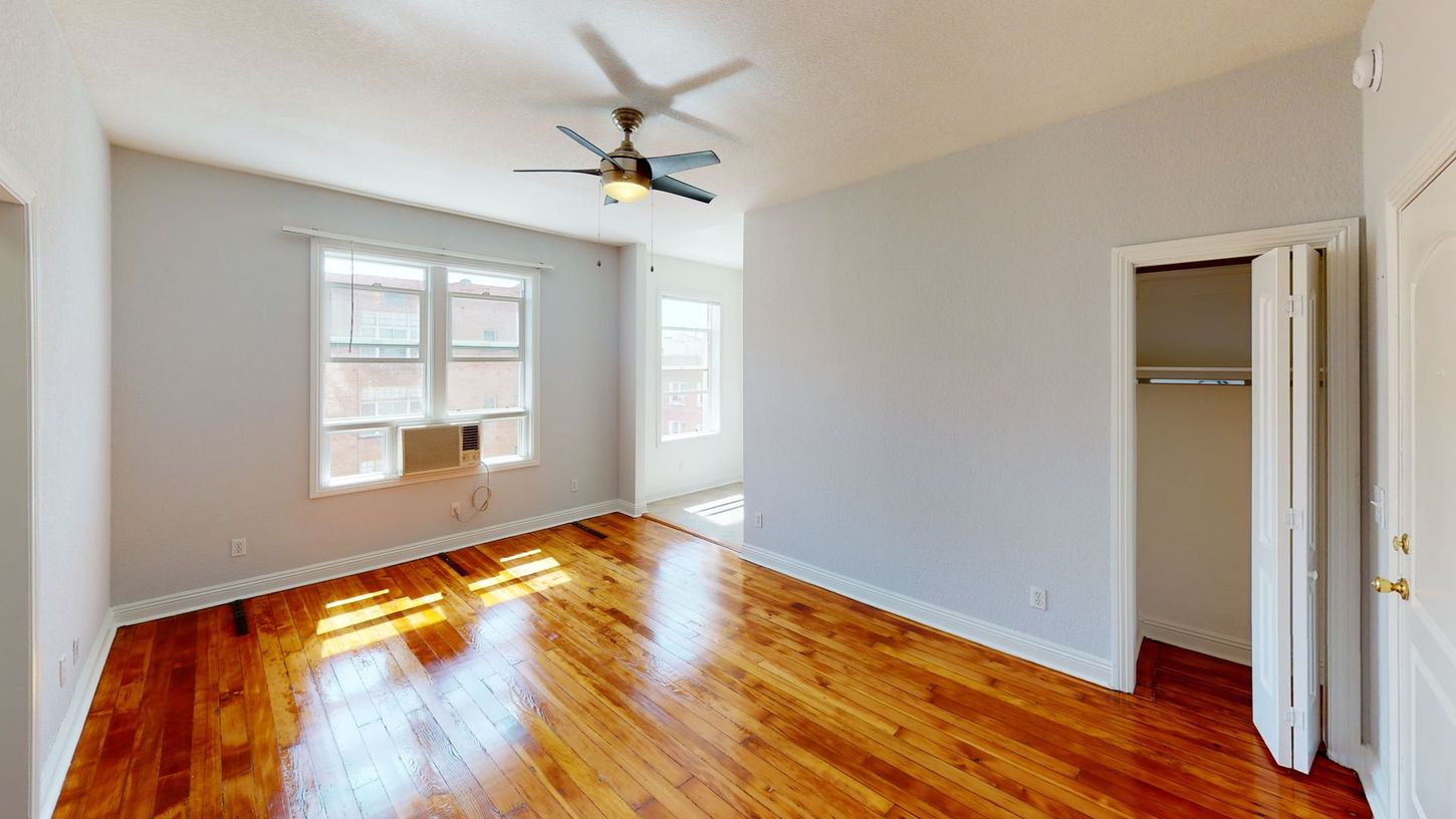 Empty room with wood floors, windows, ceiling fan, closet, and pale gray walls.