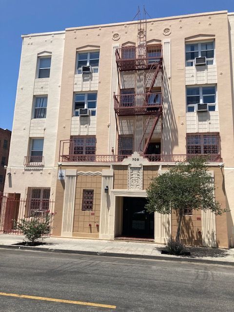 Multi-story building with fire escape, light-colored facade, windows, and a doorway.