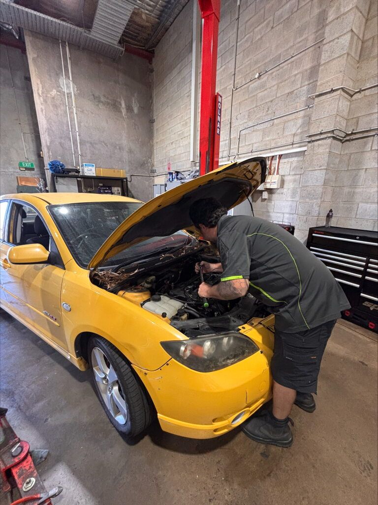 A Man is Looking Under the Hood of a Yellow Car — Kawana Auto Service In Warana, QLD