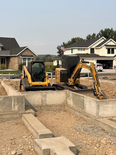 A yellow skid steer and mini excavator parked inside the concrete foundation of a house under construction.