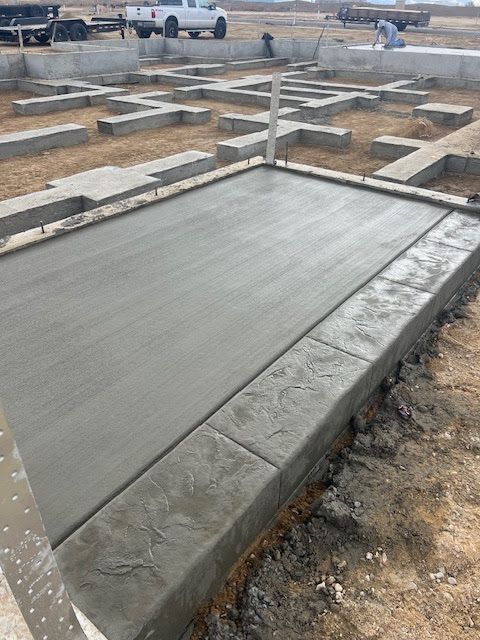 Freshly poured concrete slab with a textured border at a construction site with foundation footings in the background.