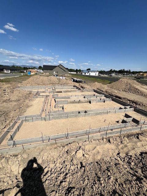 A residential construction site showing concrete foundations for a new house against a blue, clear sky.