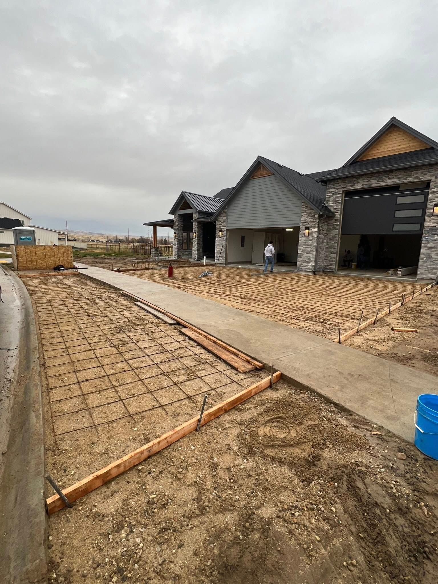 Construction site showing a house with a stone facade, open garage, and forms set up for pouring a concrete driveway.
