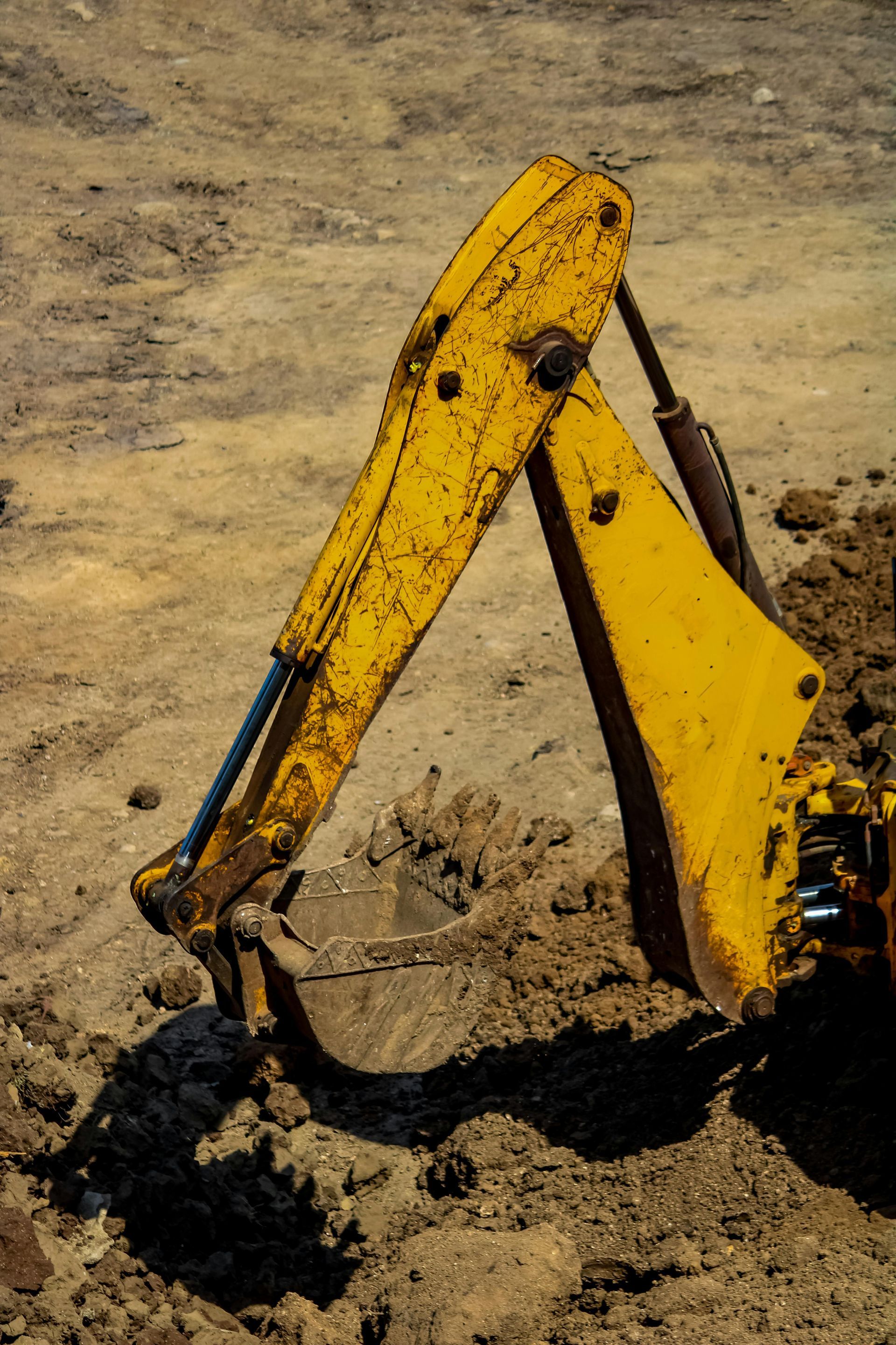 Yellow excavator arm and bucket digging into dirt at a construction site.