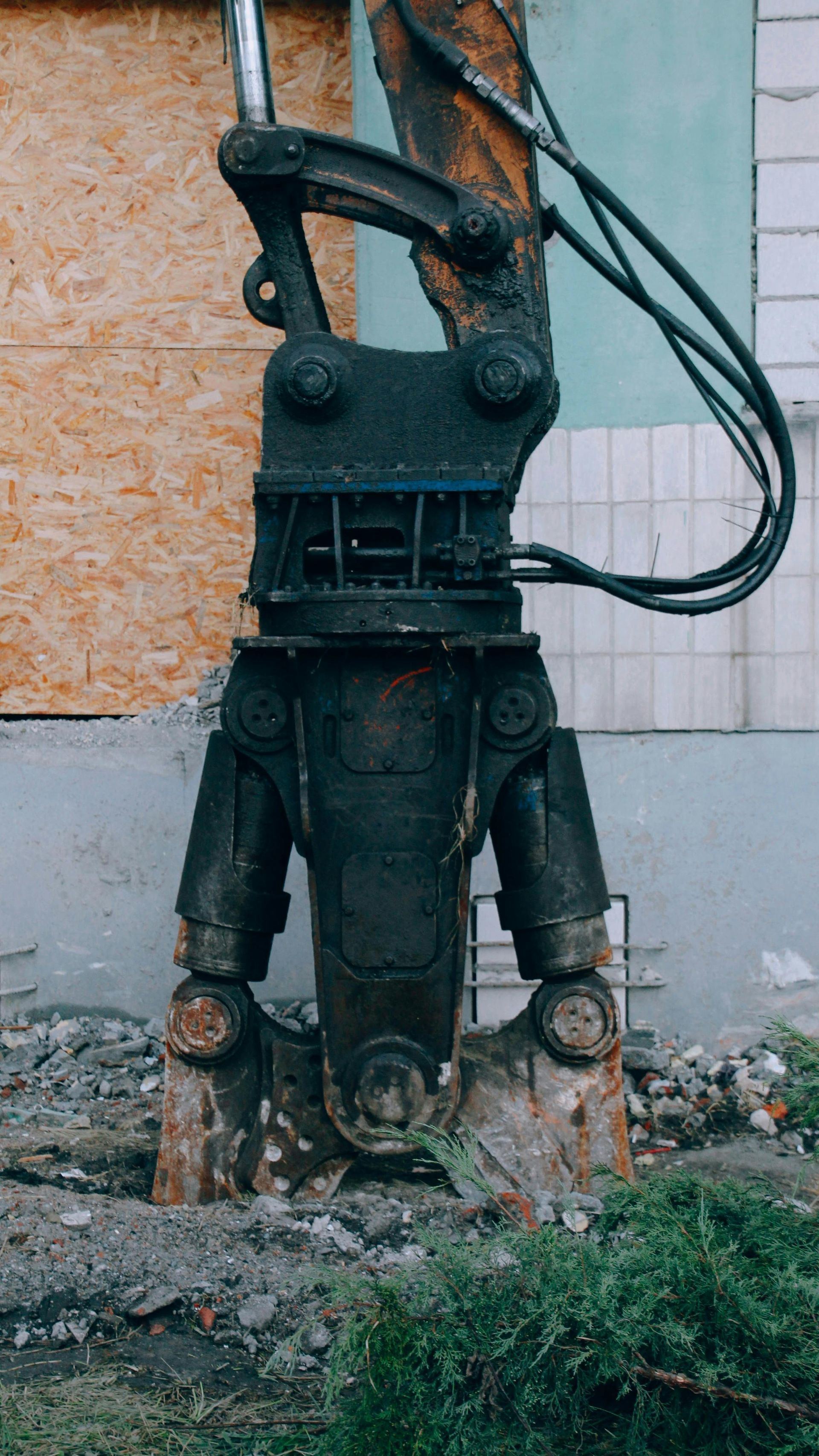 A heavy-duty hydraulic demolition shear attached to an excavator arm, positioned against a building under renovation.