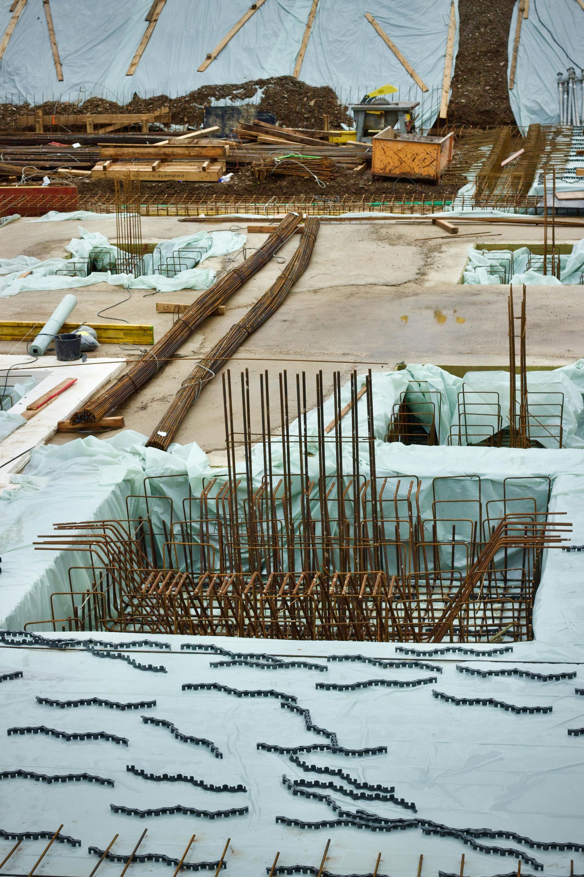 Construction site showing steel rebar reinforcement cages set into a concrete foundation under a white protective canopy.