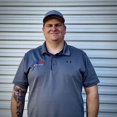 A man wearing a hat and a gray shirt is standing in front of a metal wall.