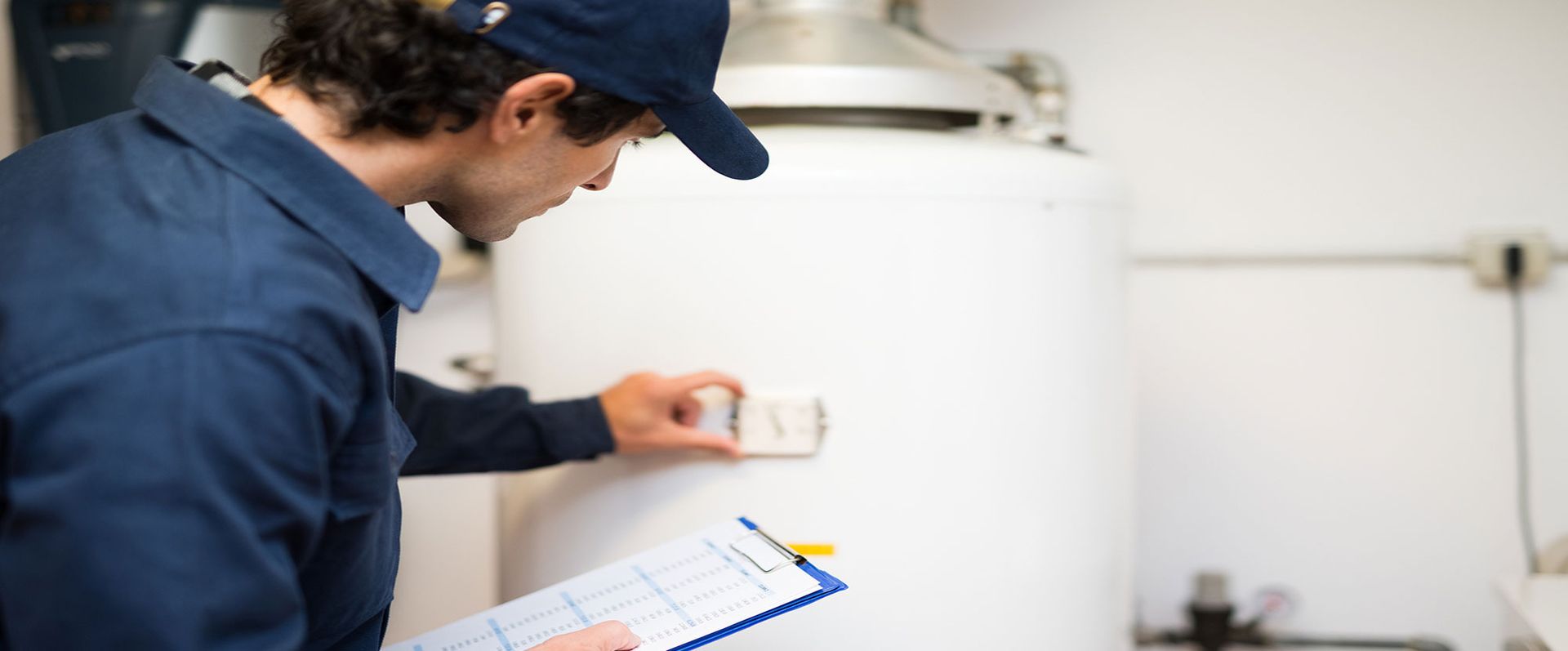 A man is looking at a water heater while holding a clipboard.