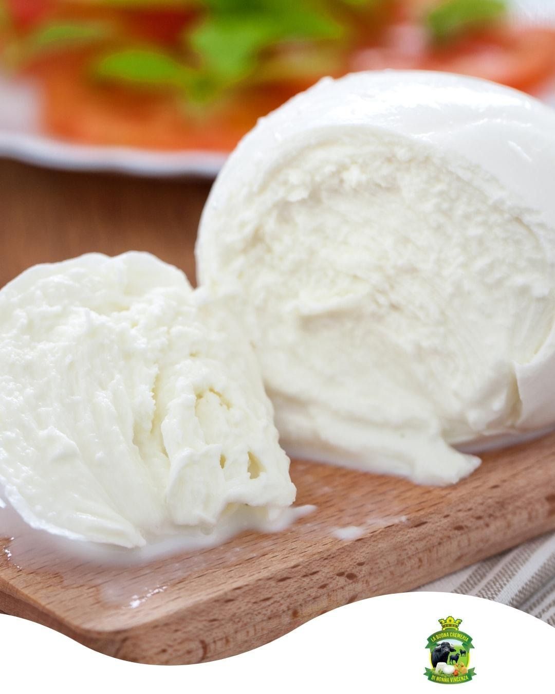 Mozzarella fresca su un tagliere di legno, bianca e cremosa, con una fetta accanto.