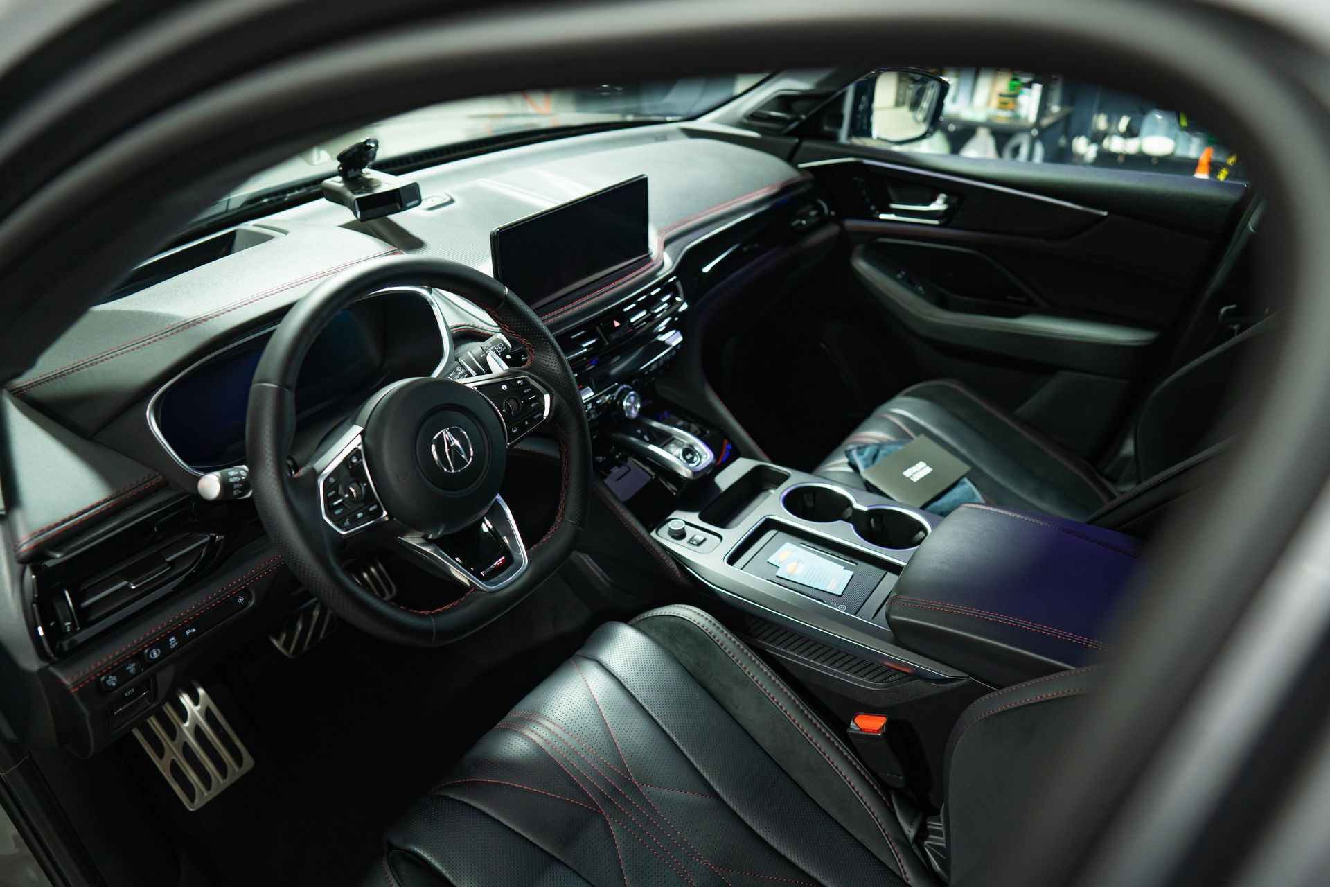 Interior view of a modern Acura vehicle cabin with a black leather steering wheel, center console, and dashboard.