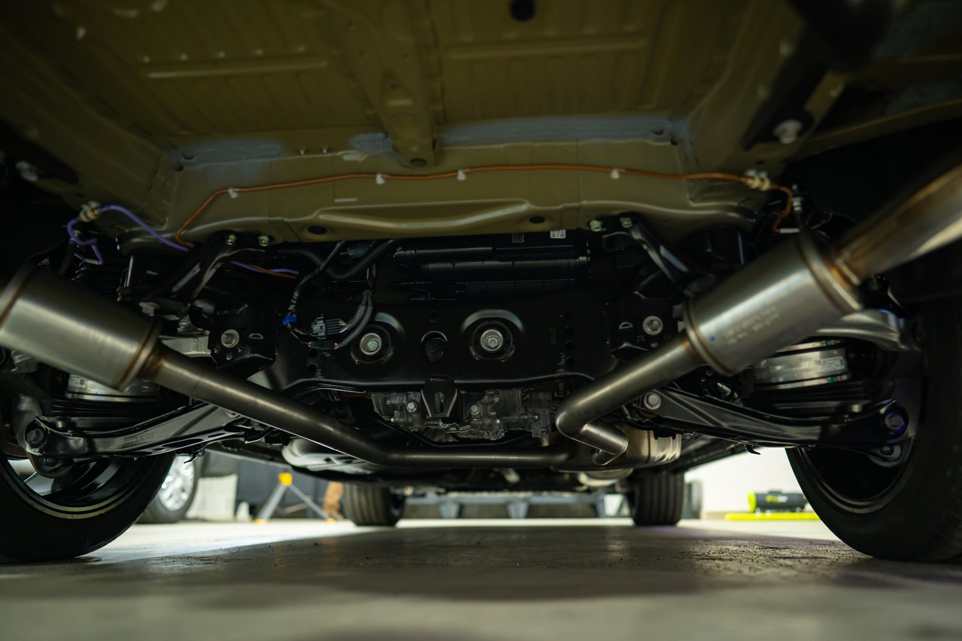 A low-angle view of the undercarriage of a car, showing the exhaust system, suspension components, and rear tires.
