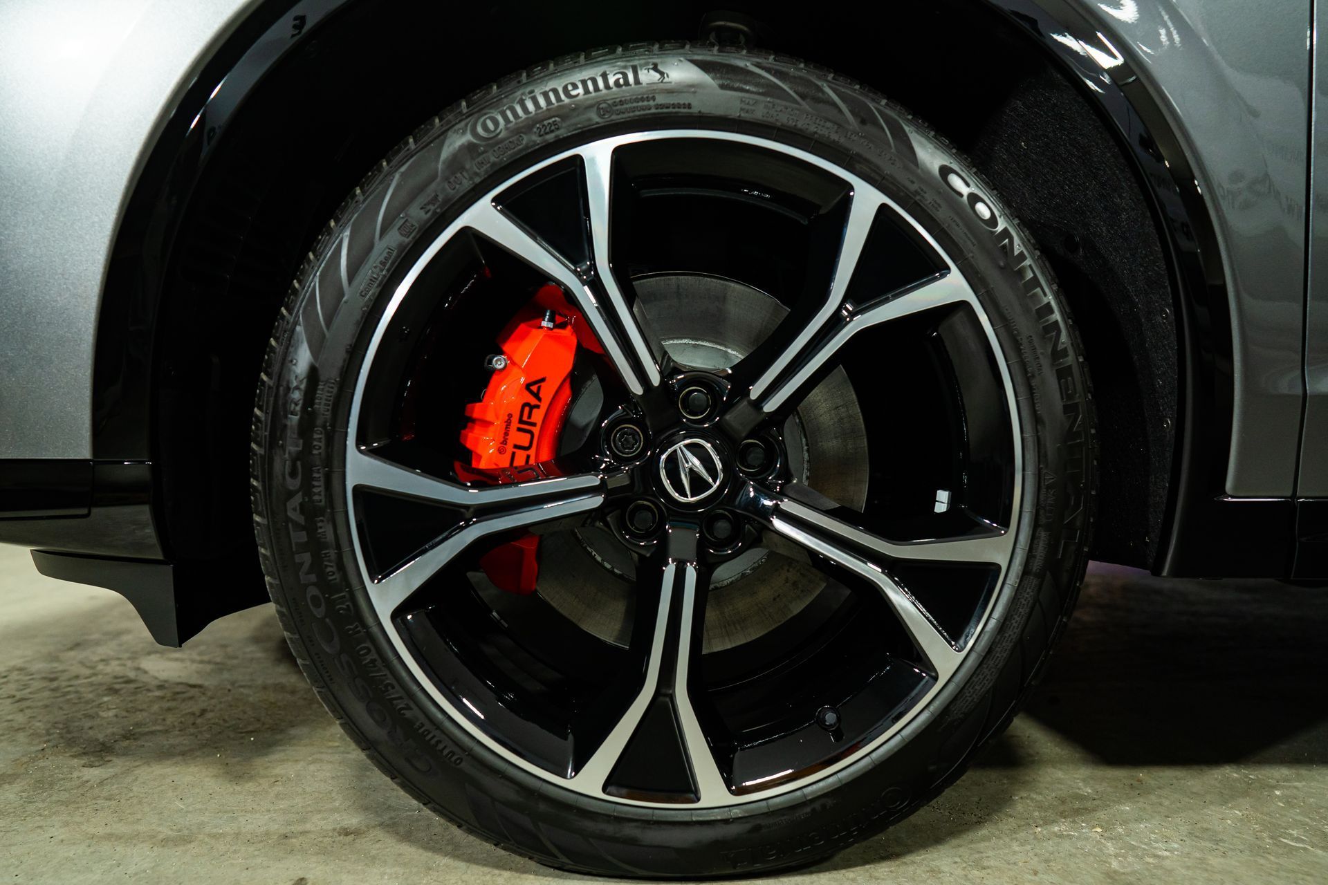 Close-up of a silver and black Acura wheel with a bright red brake caliper visible behind the spokes.