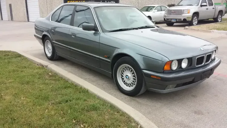A dark green BMW 5 Series sedan parked on asphalt near a patch of grass.