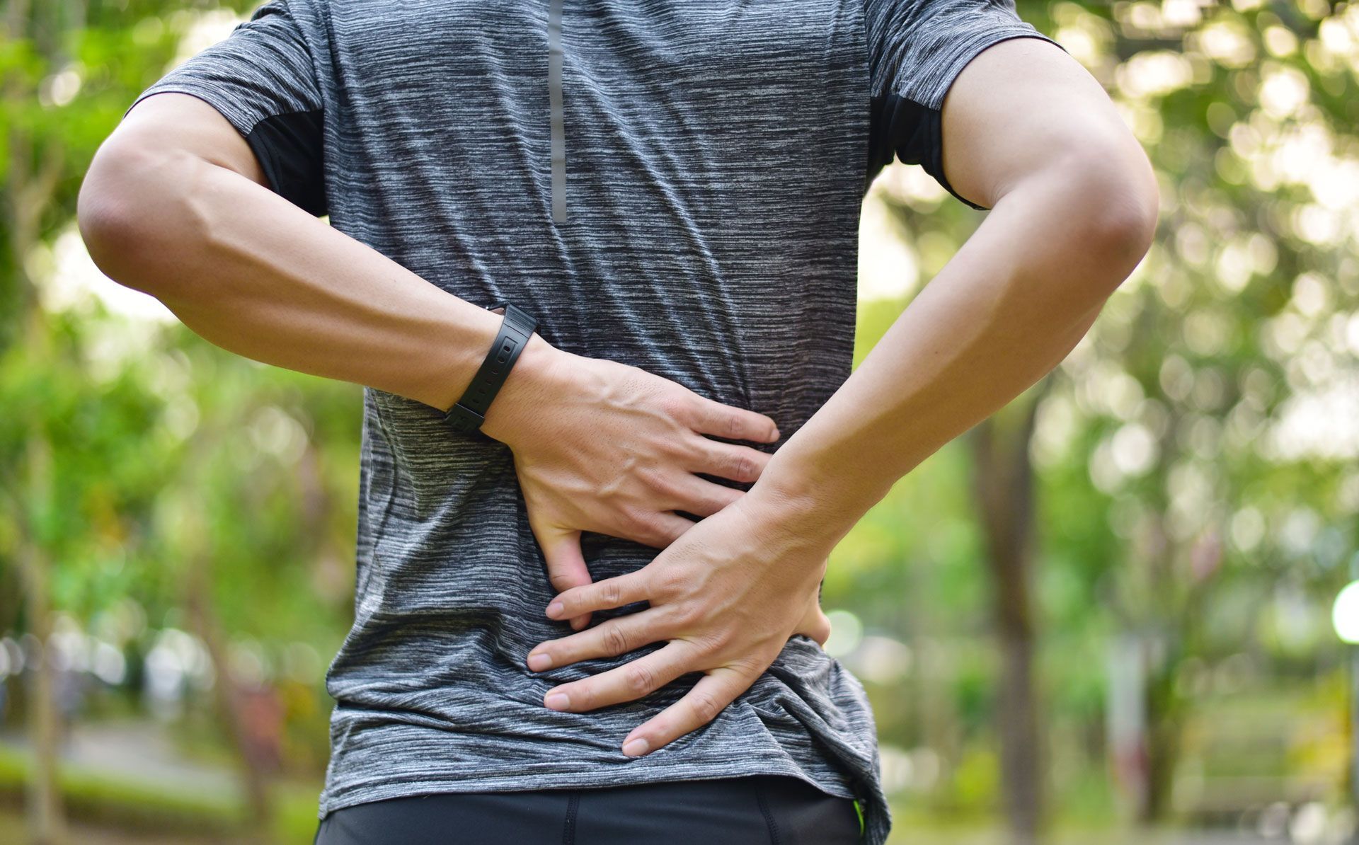 Person with hands on lower back, possibly experiencing pain outdoors.