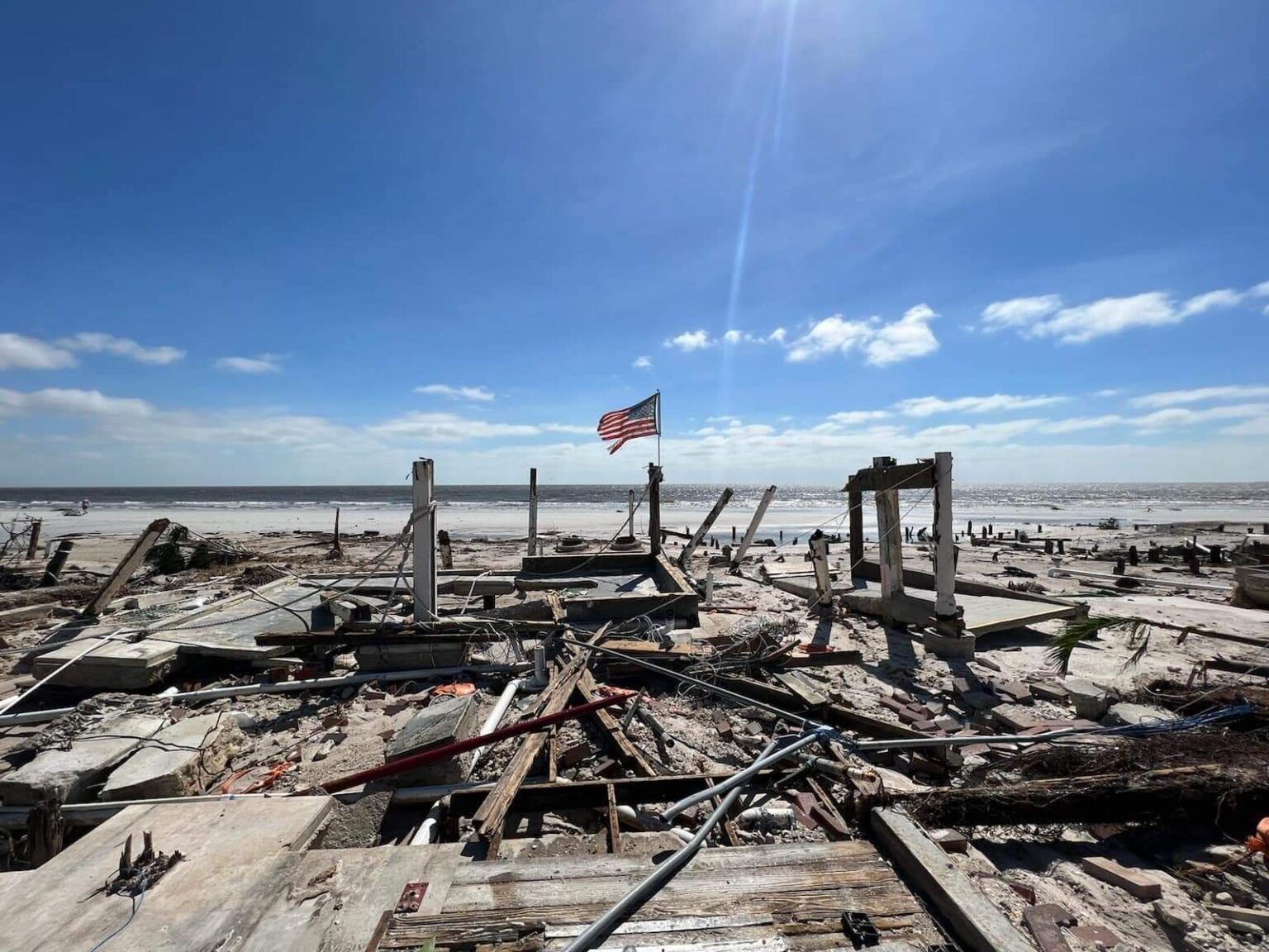A flag is flying over a pile of wood on a beach