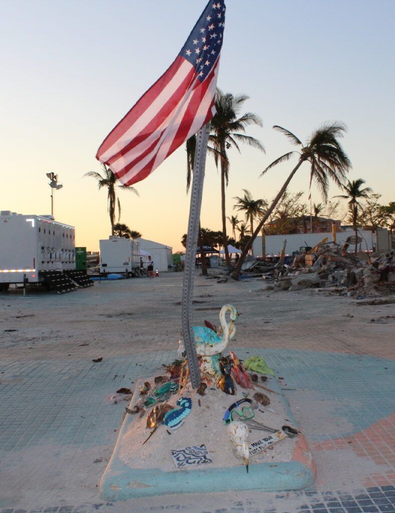 An american flag is flying in the wind in front of palm trees