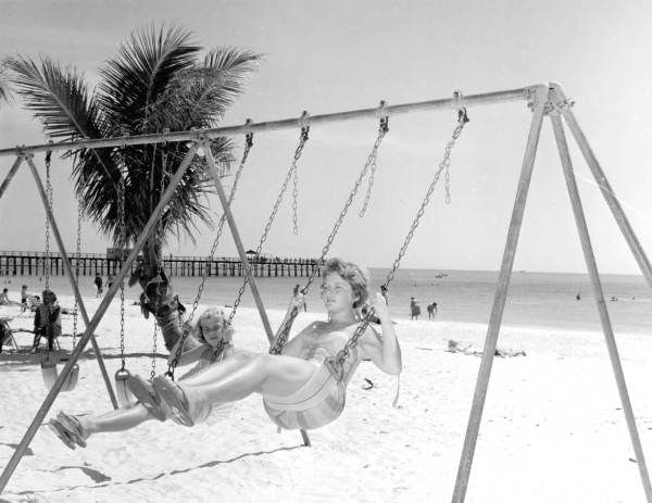 A black and white photo of people swinging on a beach