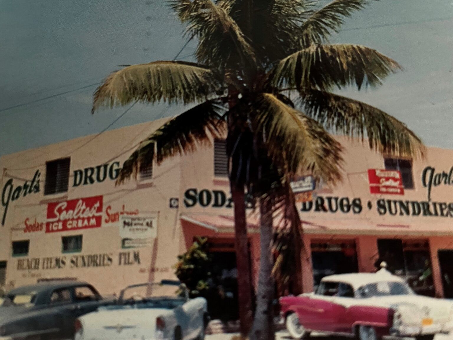 Cars are parked in front of a store that sells soda and drugs