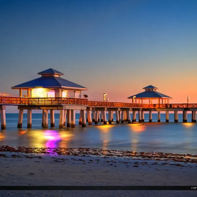 A pier is lit up at night with a sunset in the background