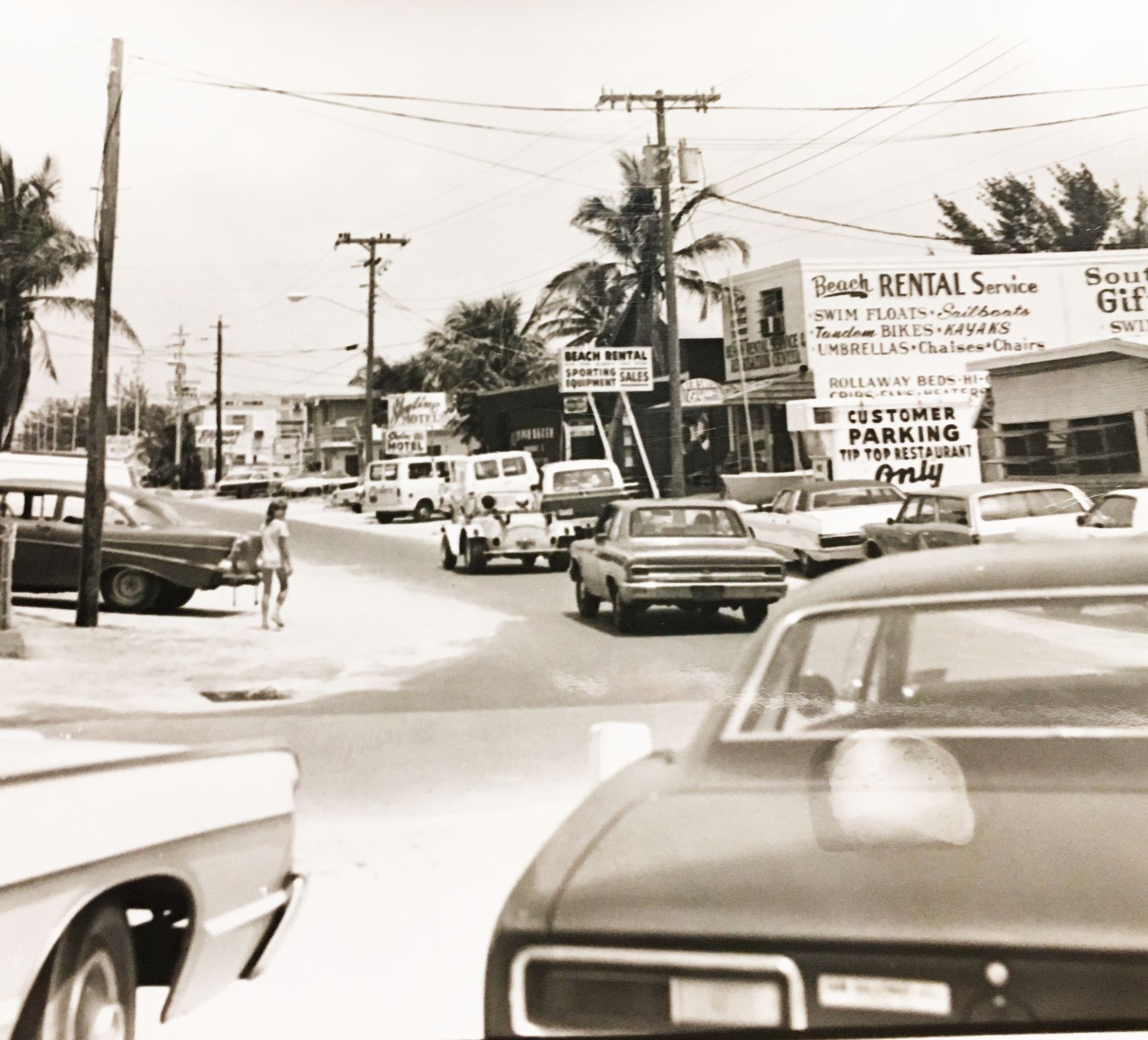 A black and white photo of a street with a rental service sign in the background