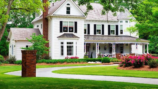 A large white house with a large porch is surrounded by trees and grass.