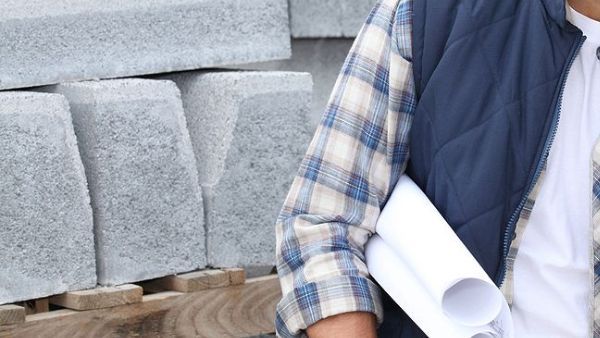 A landscape contractor in a plaid shirt is holding a roll of blueprints.