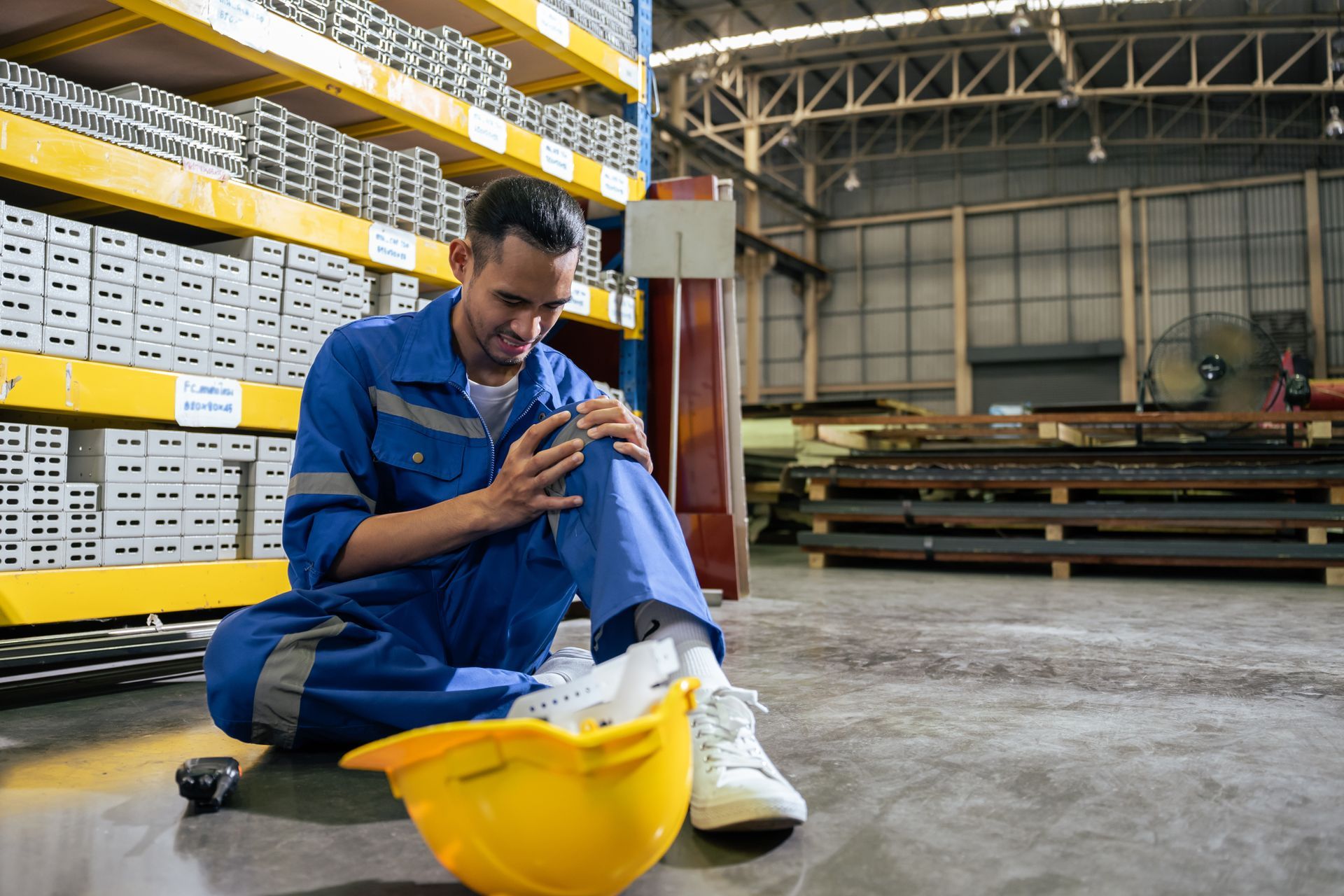 Two men in a factory setting; one points at a tablet, the other looks down, both appear focused.