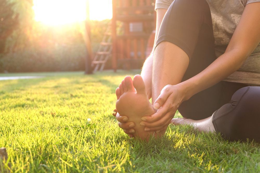 A Woman Is Sitting On The Grass Massaging Her Foot — Ocean Bliss Thai Massage In Ballina, NSW