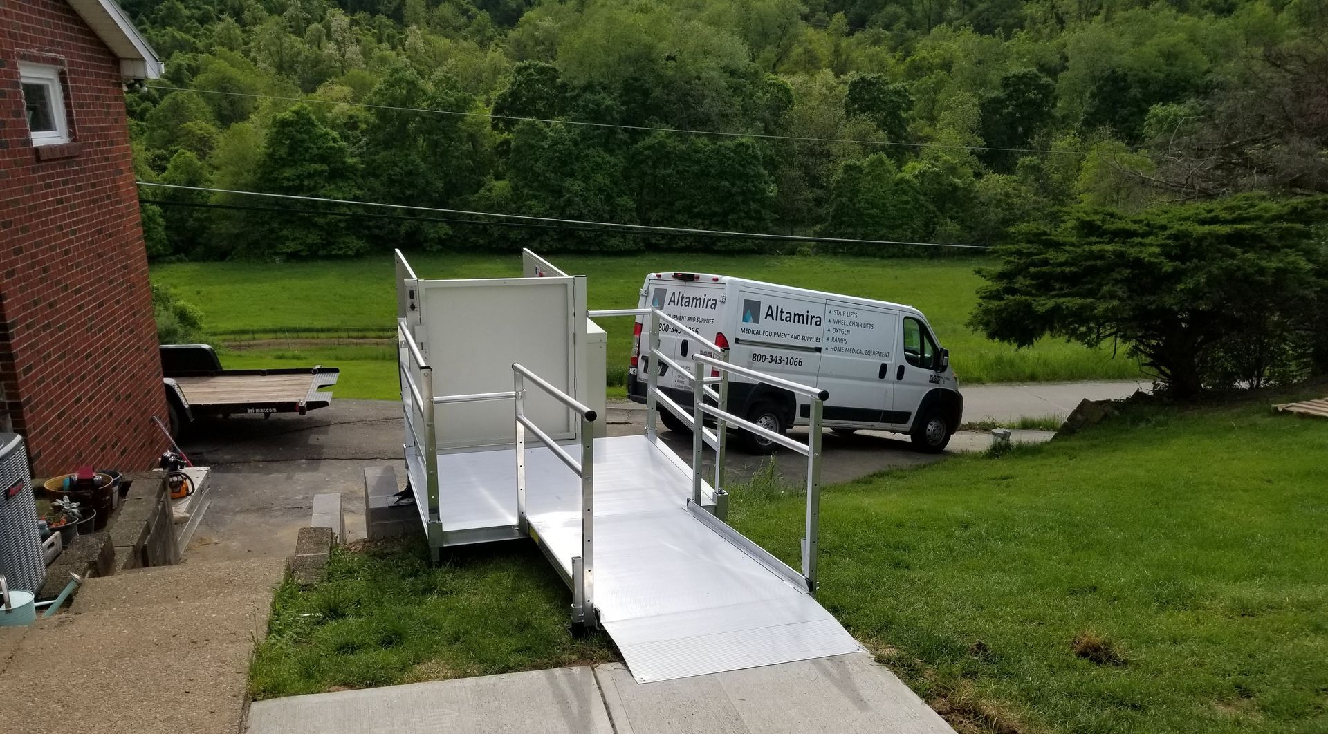 A white van is parked next to a ramp in front of a brick house.