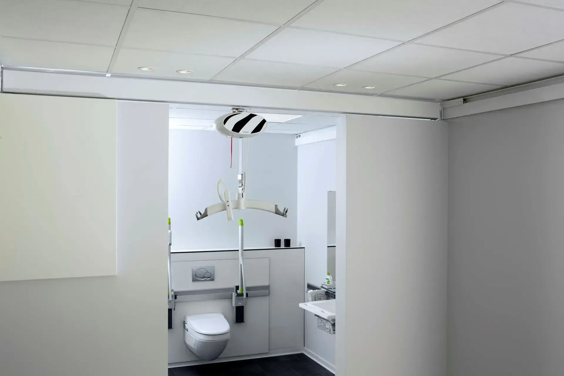 A bathroom with a toilet and a patient lift by Altamira Ltd.