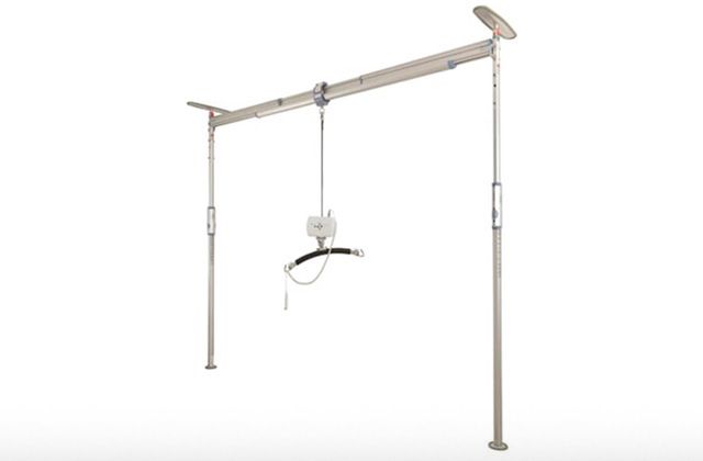 Ceiling-mounted patient lift system in a room. Beige poles and track support a lifting device with sling.