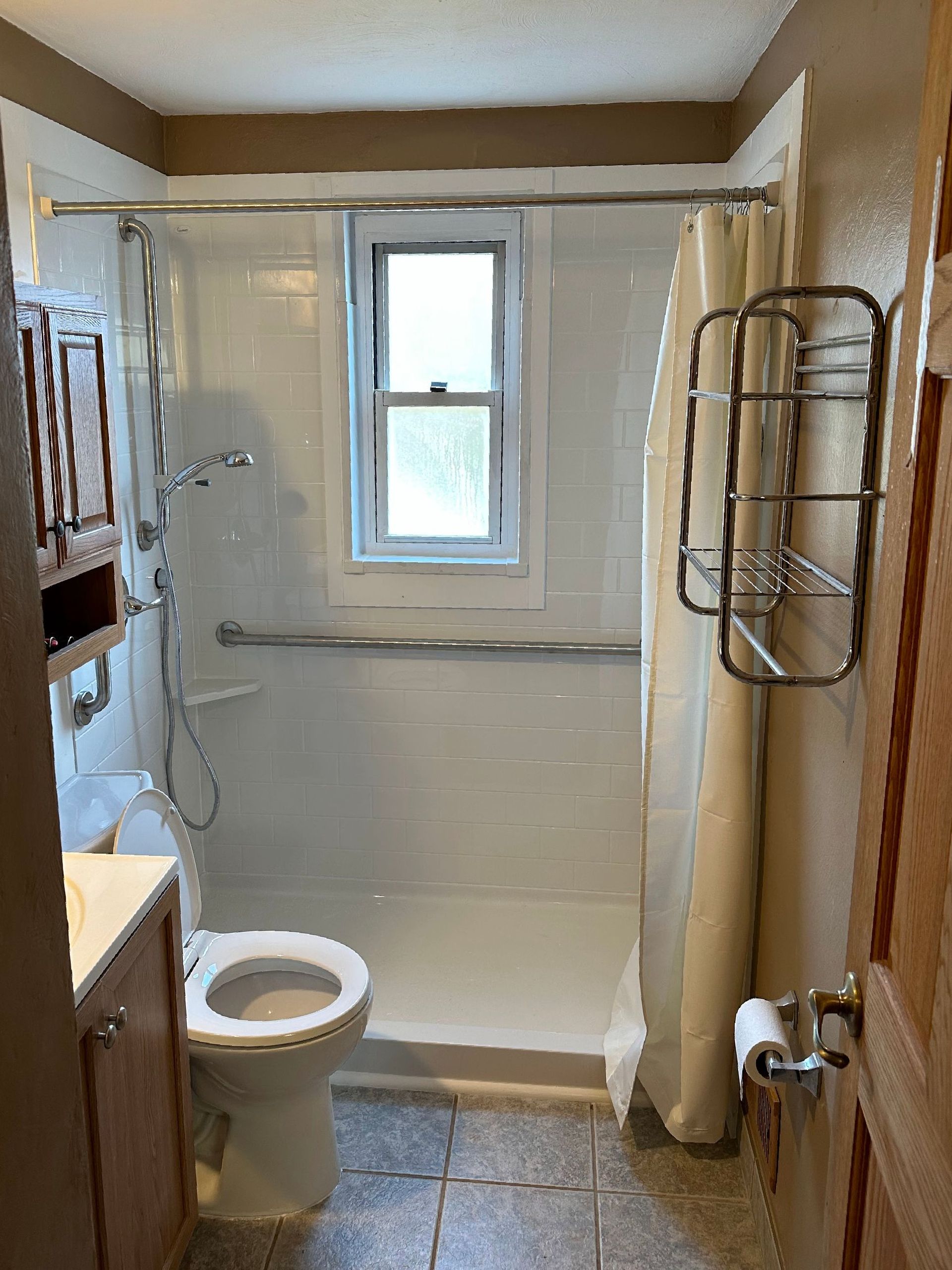 A bathroom with a toilet , sink , shower and window.