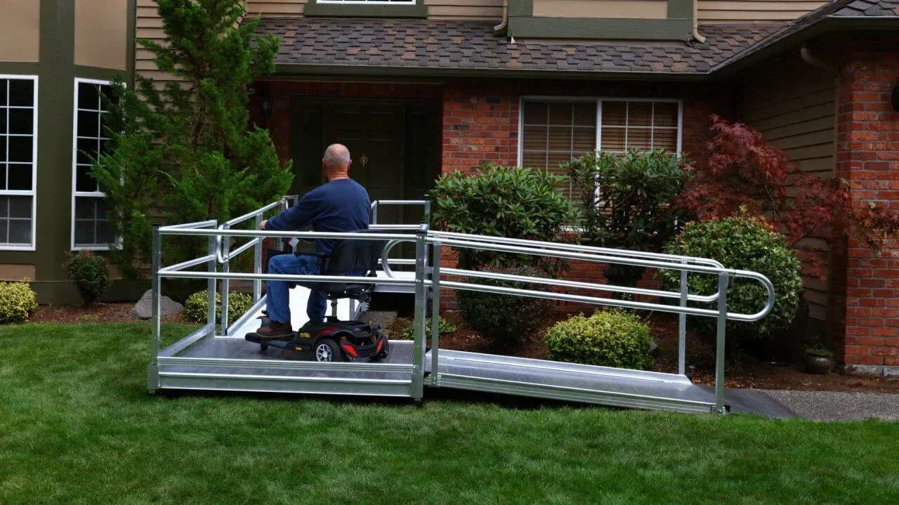 Man in wheelchair on a lift accessing the front door of a house with a ramp.