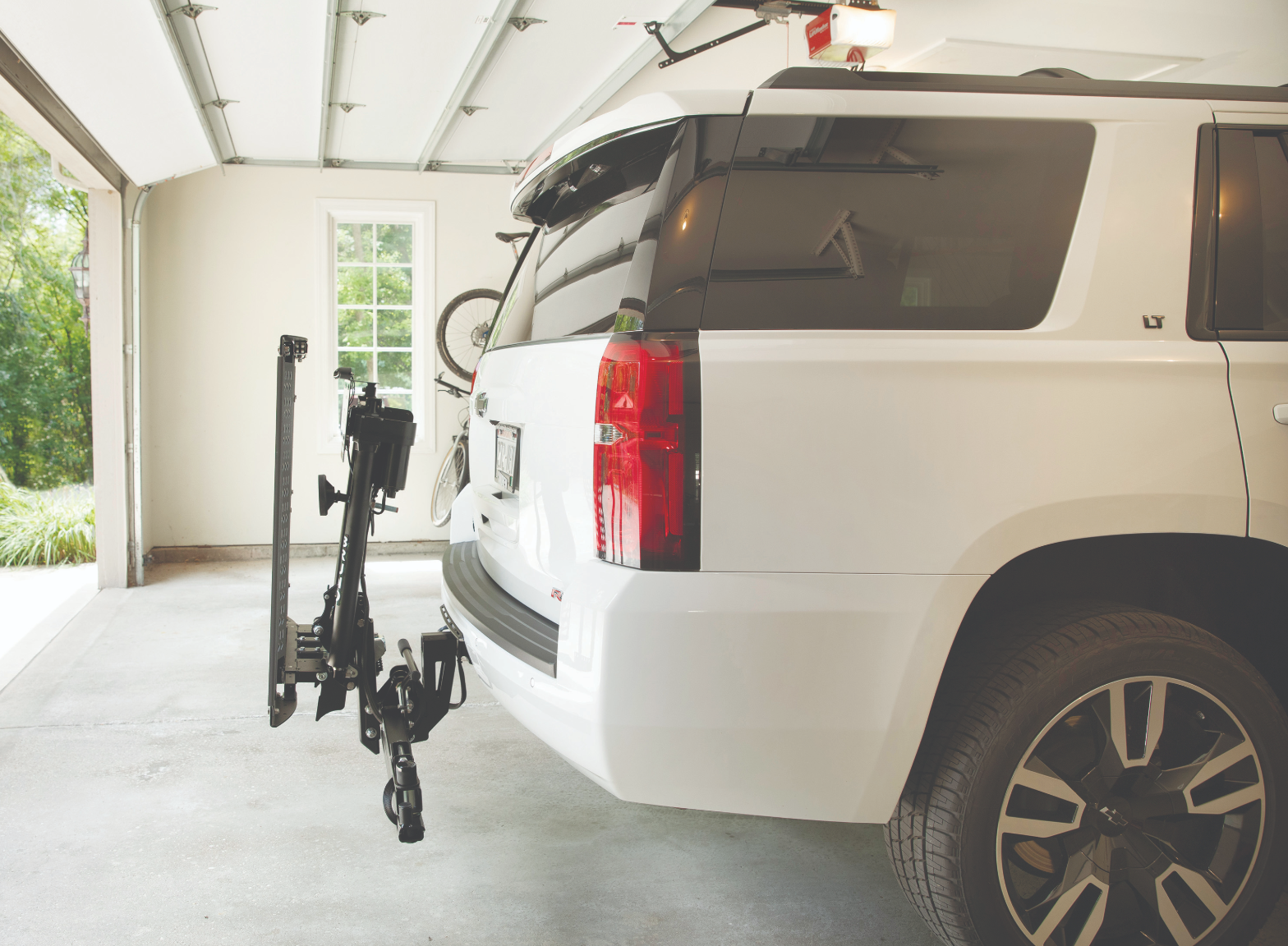 A white suv with a bike rack attached to the back is parked in a garage.