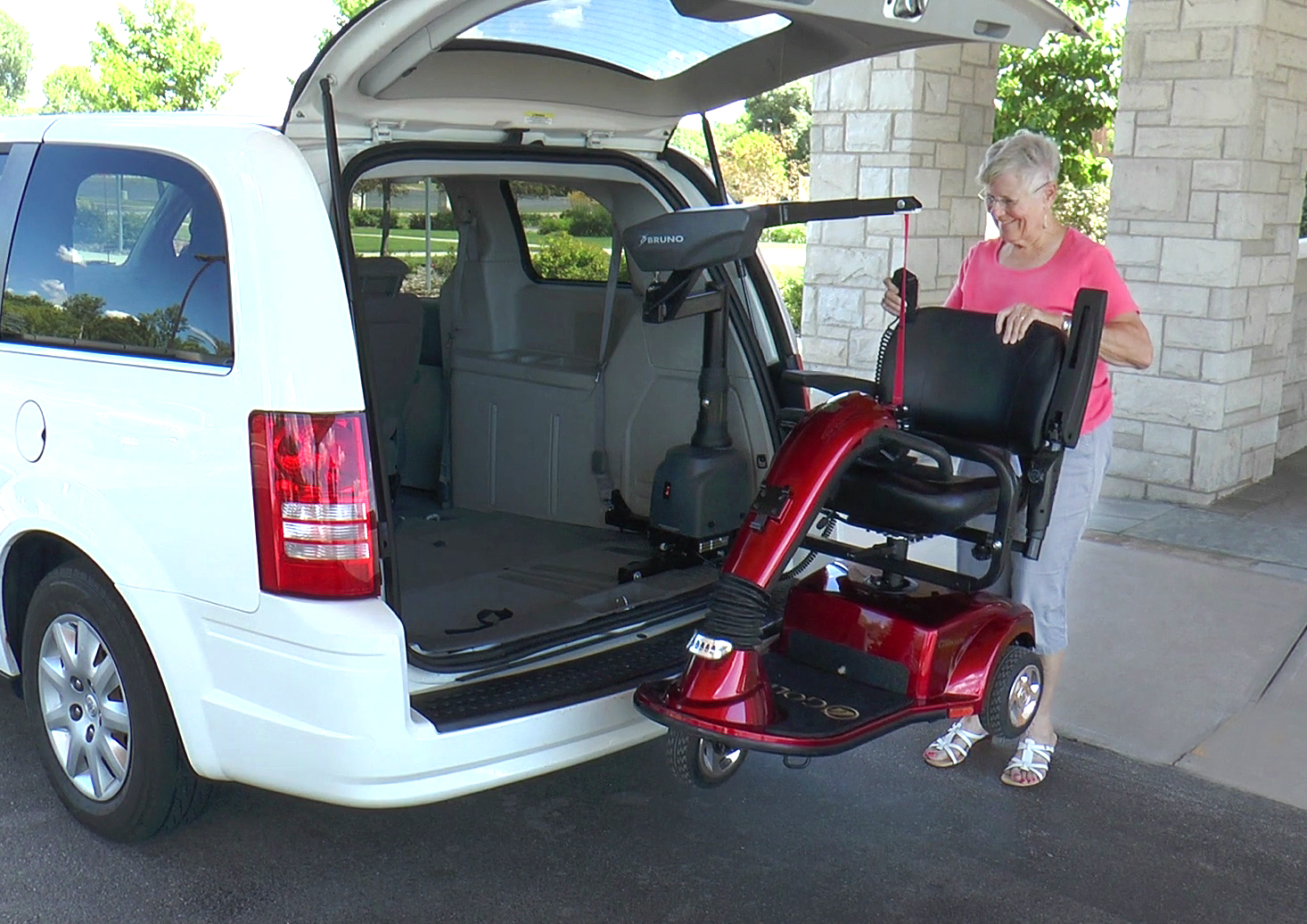 A man is loading a mobility scooter into the back of a car using a scooter lift by Altamira Ltd.