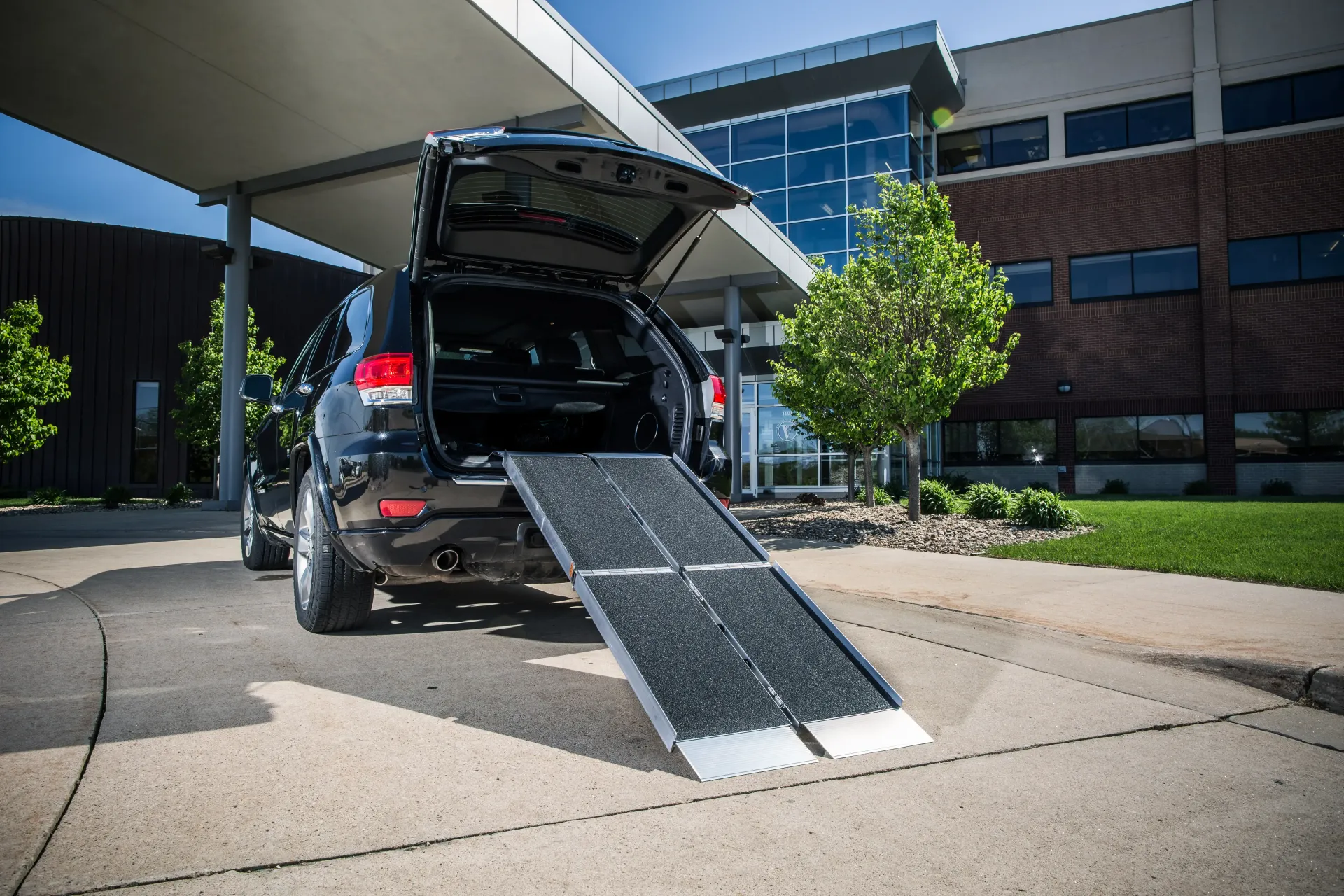 A car with a ramp in the back is parked in front of a building.