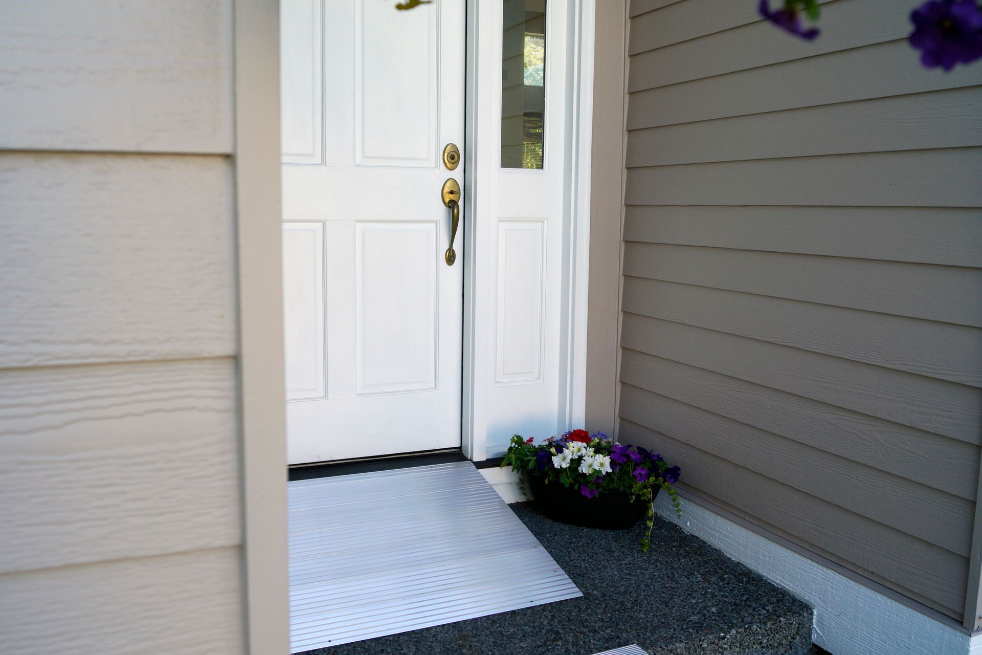 The front door of a house with a accessibility ramp and flowers on the porch