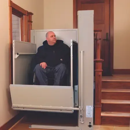 A man in a wheelchair is sitting in a vertical platform lift by Altamira Ltd.