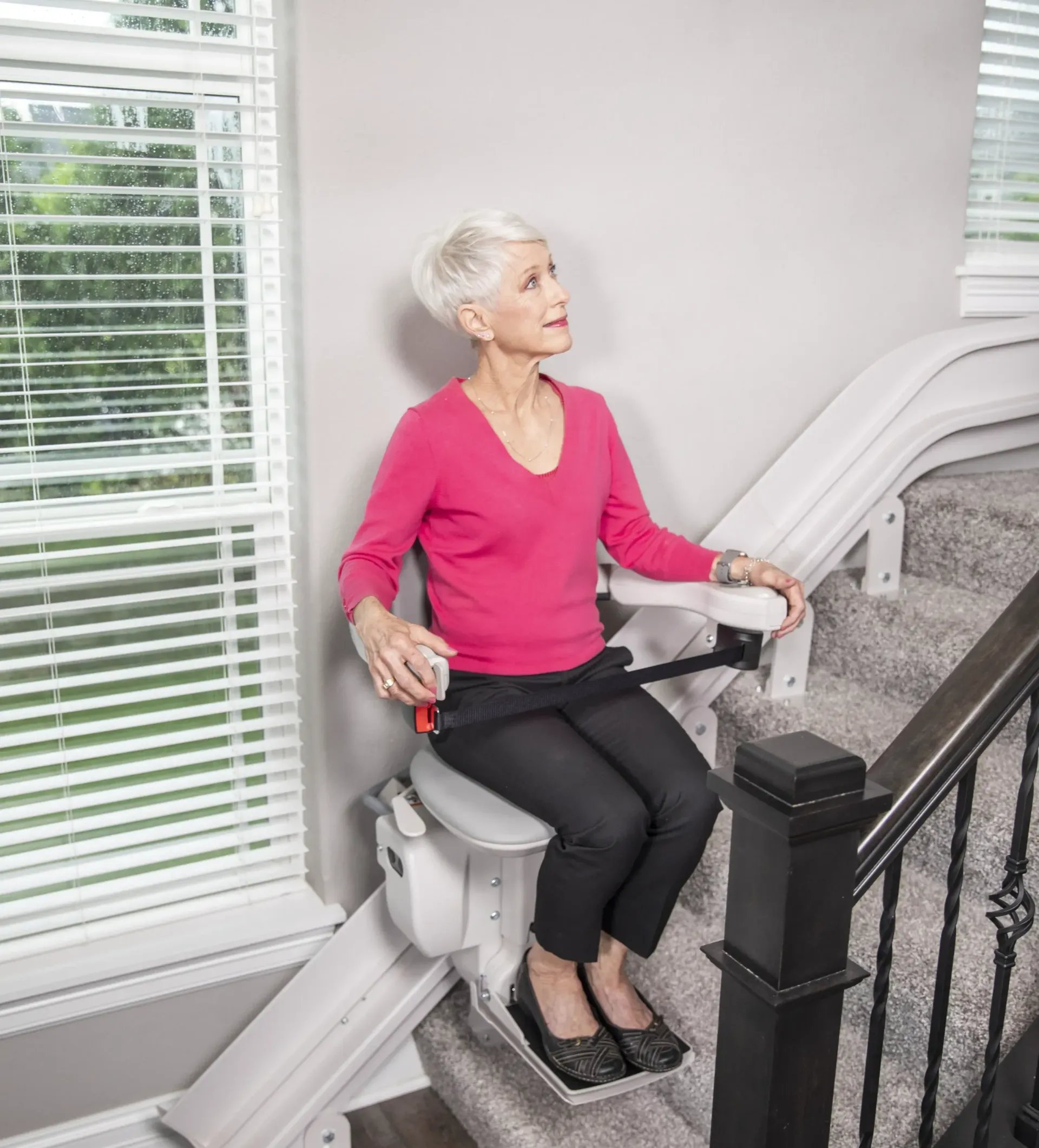 An elderly woman is sitting on a Bruno curved indoor stairlift installed by Altamira Ltd.