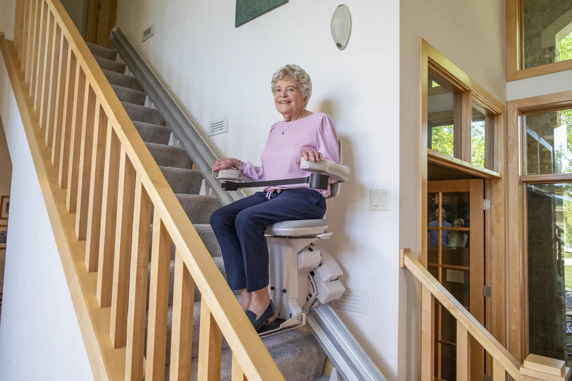 An elderly woman is sitting on a stair lift with a dog.