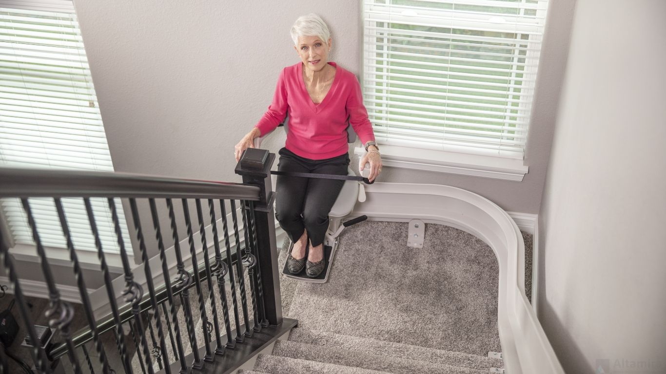 An elderly woman is sitting on a curved indoor stair lift by Altamira Ltd.