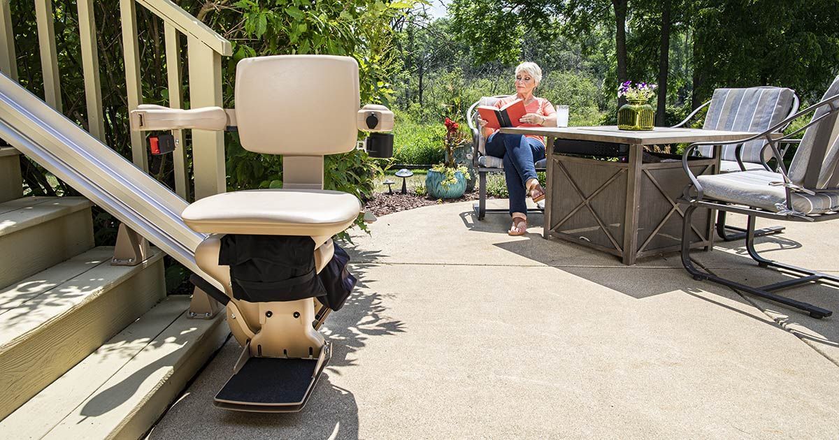 An elderly woman is sitting at a table on a patio next to an outdoor stair lift by Altamira Ltd.