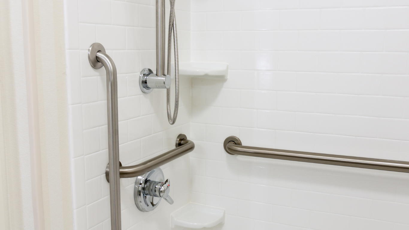 A bathroom with stainless steel handrails and a shower head.