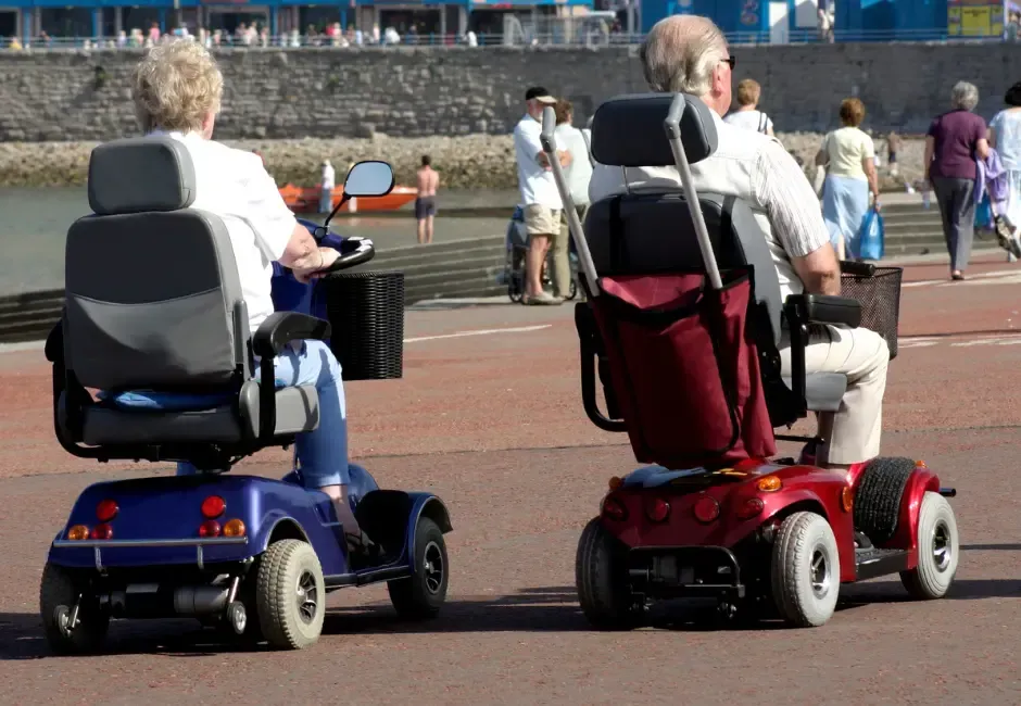 Two people are riding mobility scooters on a road