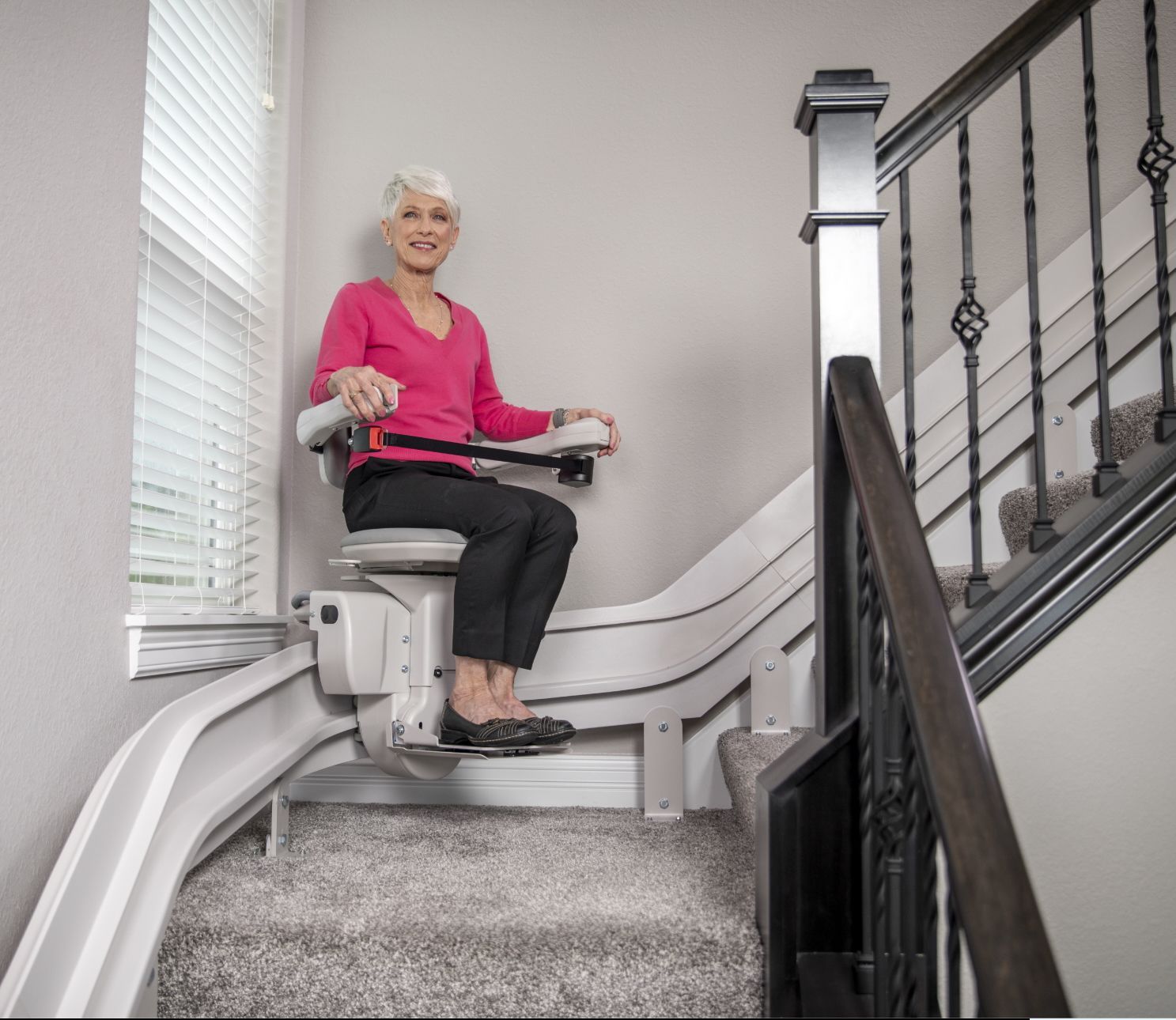 A woman in a pink shirt is sitting on a stair lift.