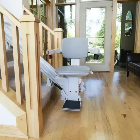 A Bruno stairlift in a living room next to stairs by Altamira Ltd.