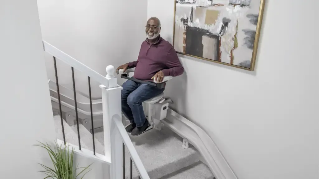 A man is sitting on a curved indoor stair lift on a set of stairs installed by Altamira Ltd.