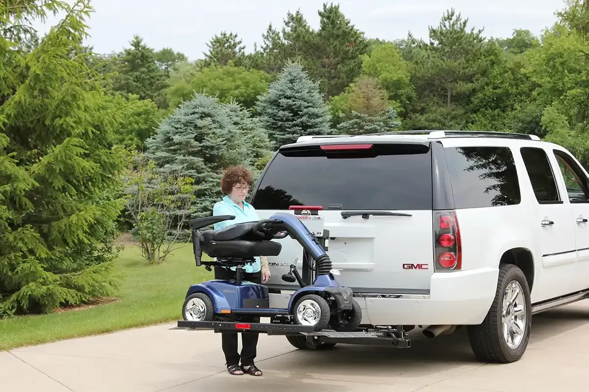 A woman is loading a mobility scooter into the back of a suv.
