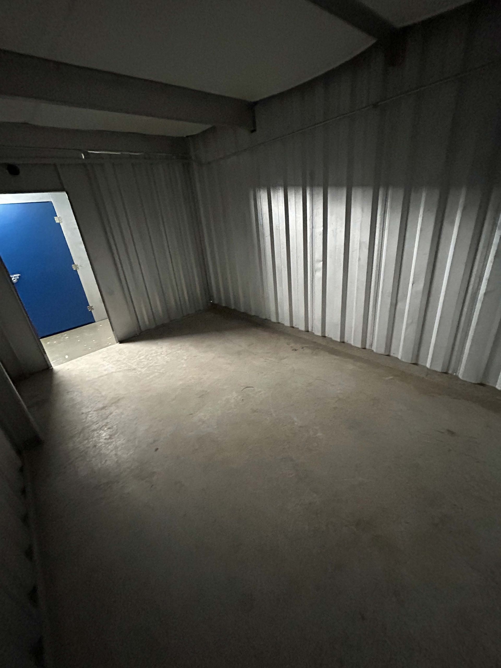 Orange dumpster filled with debris on green grass next to a road, tree, and parked cars.