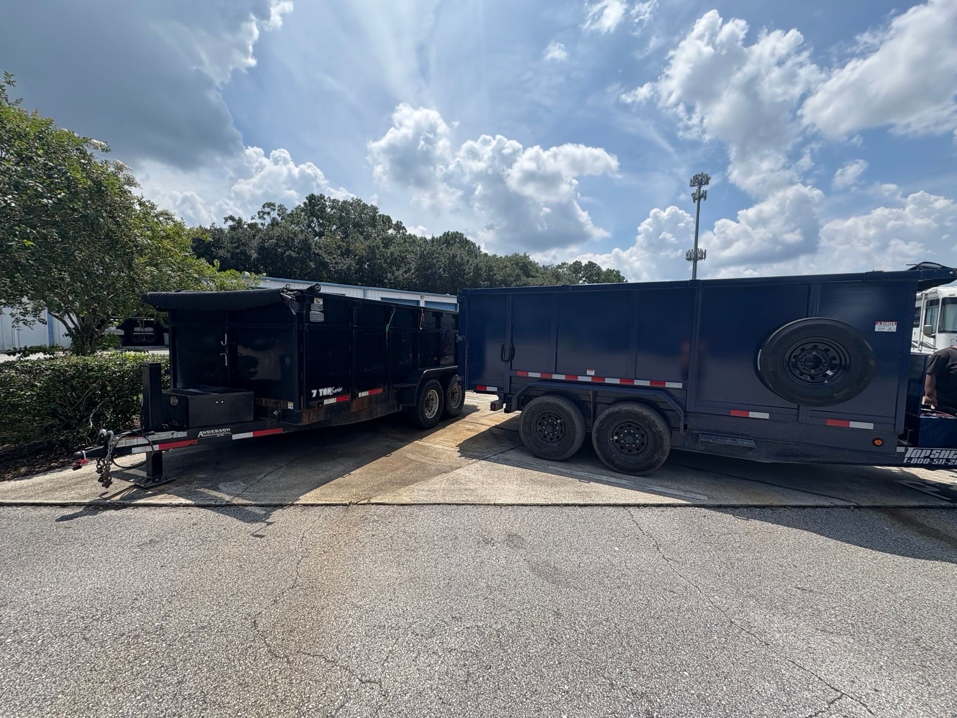 Blue dumpster filled with debris being hauled away by a truck, parked in front of a residential building.